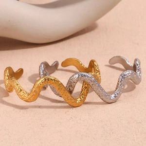 Macro detail of wave-shaped open bangles with hammered texture in gold and silver finish