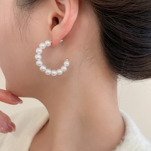 Macro side view of C-shaped pearl earrings with gold spacers worn by model