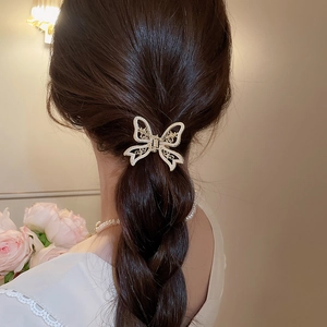 Detailed view of a golden hollow butterfly hair claw with pearls on a low ponytail