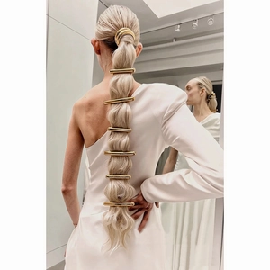 Detail of sleek gold metal hair clips and ponytail cuff shown on a model in a mirror