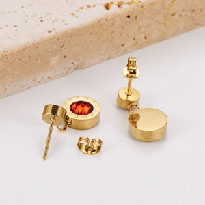Macro detail of gold stud earring featuring a red crystal and Roman numeral engraving