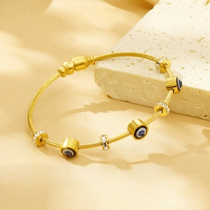 Detailed close-up of a gold-tone evil eye bangle with crystals on a textured stone