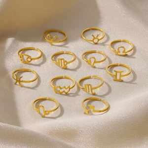 Collection of twelve gold zodiac symbol open rings on beige satin fabric surface
