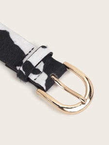 Close-up of black and white cow print leather belt with gold oval metal buckle