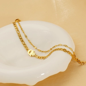 18K gold plated stainless steel layered bracelet with Hamsa charm on a ceramic plate