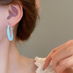 Close-up of light blue polished hoop earrings worn by a model in warm sunset lighting