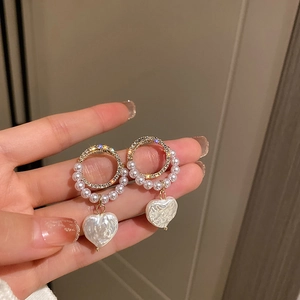 Detail of heart-shaped pearl earrings with sparkling crystal hoop in golden finish