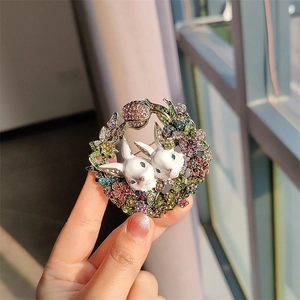 Vintage rabbit brooch featuring white enamel bunnies and colorful rhinestone floral wreath
