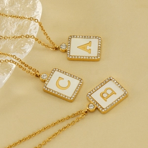 Square shell initial necklace with zircon gold frame on elegant yellow silk background