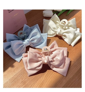Detail of oversized satin bow hair claws in light blue, beige, and pink colors