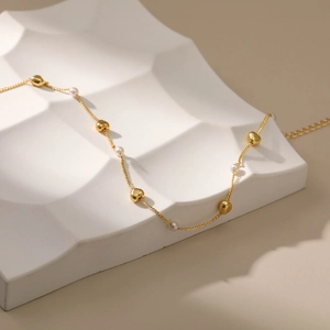 Elegante Goldhalskette mit Herzanhängern und kleinen Perlen auf einem Wellentablett