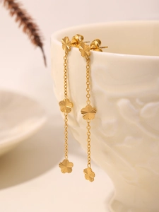 Detail of gold floral tassel earrings hanging on a white textured ceramic cup