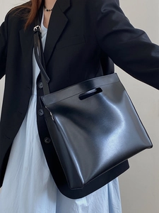 Minimalist black leather tote bag with top handle and shoulder strap shown on a model