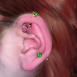 Close-up of titanium steel ear piercing set with green zircon and golden studs on ear