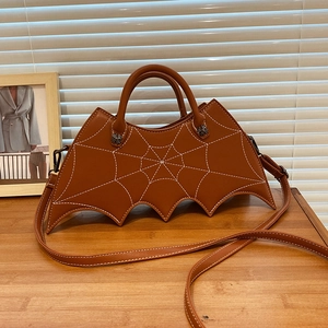 Brown leather bat-shaped bag featuring white spider web embroidery on a wooden table
