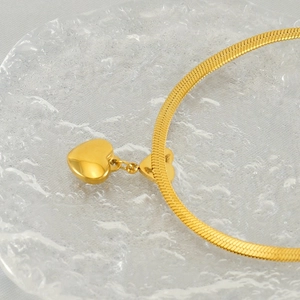 Collier avec pendentif cœur doré et chaîne serpent sur plat en verre