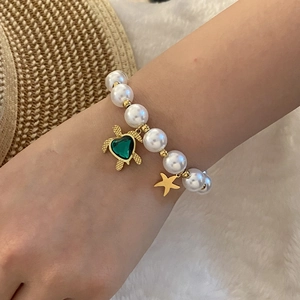 Beaded pearl bracelet with gold turtle charm and green gem on a cozy resort background