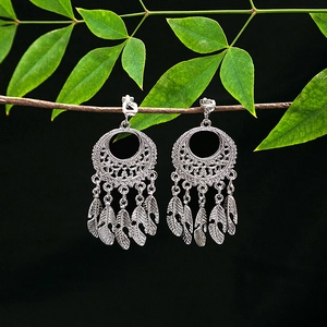 Close-up of Bohemian silver feather tassel earrings hanging on a natural green leaf