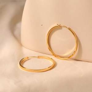 Macro shot of large 18K gold-plated brass hoop earrings on a minimalist beige background