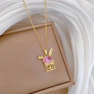 Detailed shot of golden rabbit pendant with pink gemstones on brown gift box and silk