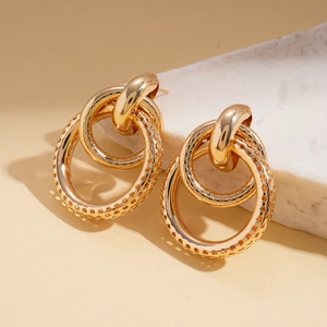 Detailed view of gold interlocking hollow rings earrings on stone over beige background