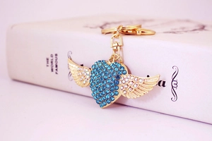 Detail of gold heart keychain with blue crystals and rhinestone wings on a book