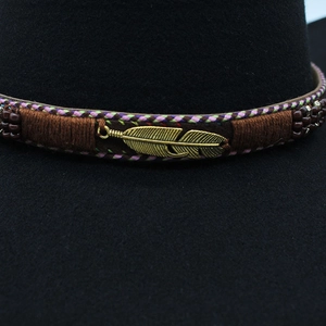 Close-up of golden feather charm and ethnic embroidery on white fedora hat band