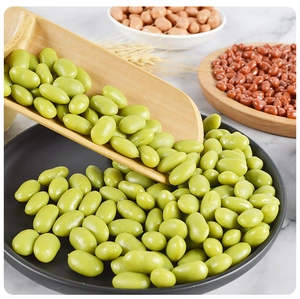 Realistic faux green soybeans poured from a wooden shovel into a black ceramic plate