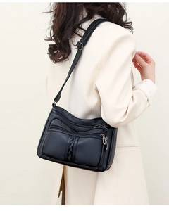 Detail of black pebbled leather crossbody bag with multiple zippers and woven texture