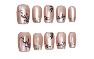 Macro view of short square rose gold cat-eye press-on nails with black leaf motifs
