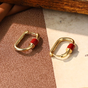Detail of gold rectangular earrings with red enamel cylinder charms on textured paper