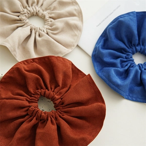 Detailed view of large fabric scrunchies in beige, rust red, and navy blue with soft textures