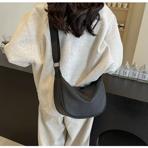 Rear view of a model wearing a large black nylon crescent crossbody bag in a cafe