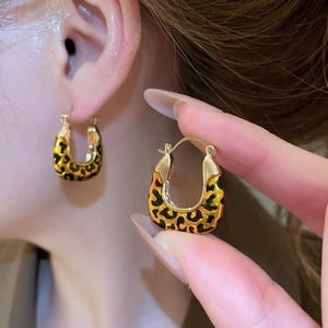 Close-up of gold U-shaped leopard print earrings shown on ear and held by hand