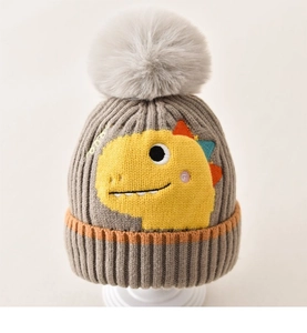 Detail of grey knitted baby hat featuring yellow dinosaur embroidery and fluffy pompom