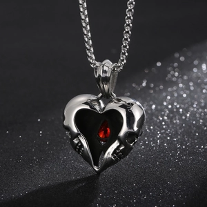 Macro detail of punk heart pendant with two skulls and a red gemstone on metal chain