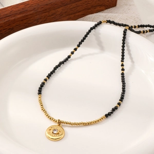 Minimalist black spinel evil eye beaded necklace with gold accents on ceramic tray