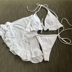 Vista dettagliata del bikini a tre pezzi bianco con gonna in mesh a balze su fondo scuro