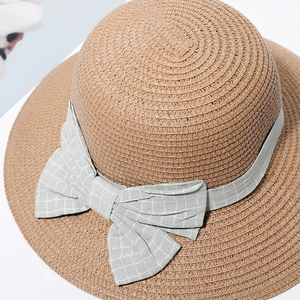 Detail of a brown wide-brim straw hat featuring a grey plaid bow ribbon decoration