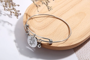 Detail of adjustable silver steel wire bracelet with engraved charm and small round bell