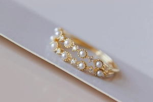 Detail shot of a luxury gold ring with small pearls and crystals on a soft gray surface
