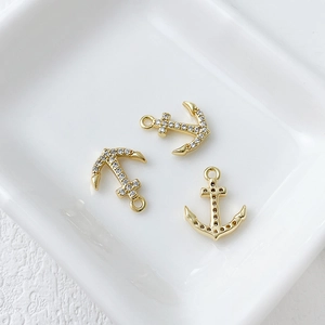 Close-up of three 14k gold plated micro-pave anchor charms in a white ceramic tray