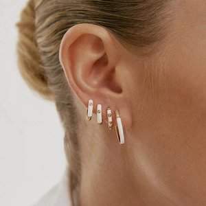 Detail of white enamel hoop earrings with gold trim and zircon on woman's ear