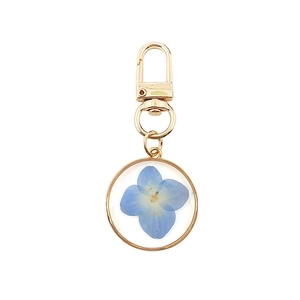 Detailed view of forget-me-not blue dried flower pendant on golden resin keychain