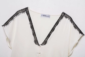 Detail eines weißen Satin-T-Shirts mit V-Ausschnitt, schwarzer Spitze und Markenetikett