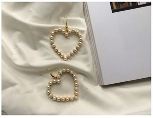 Detail view of heart-shaped gold pearl earrings on elegant white silk fabric background