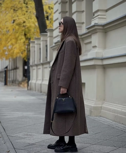 Detail of elegant long brown wool coat paired with a chic black leather handbag