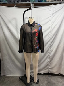 Dettaglio della camicetta in chiffon nero trasparente con stampa floreale e bottoni frontali