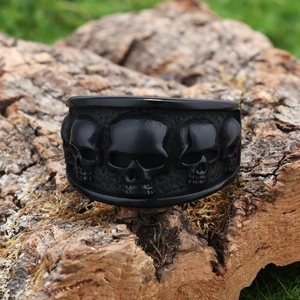 Detail of a matte black skull ring on a wood base with a rugged gothic aesthetic
