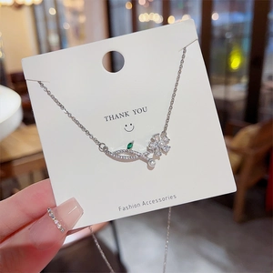 Detailed shot of silver necklace with green gemstone, floral pendant and white pearl